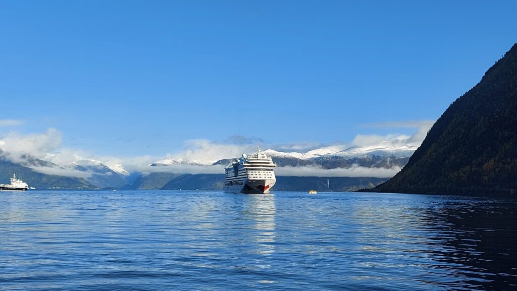 Kreuzfahrtschiff in einem sonnigen Fjord vor schneebedeckten Bergen